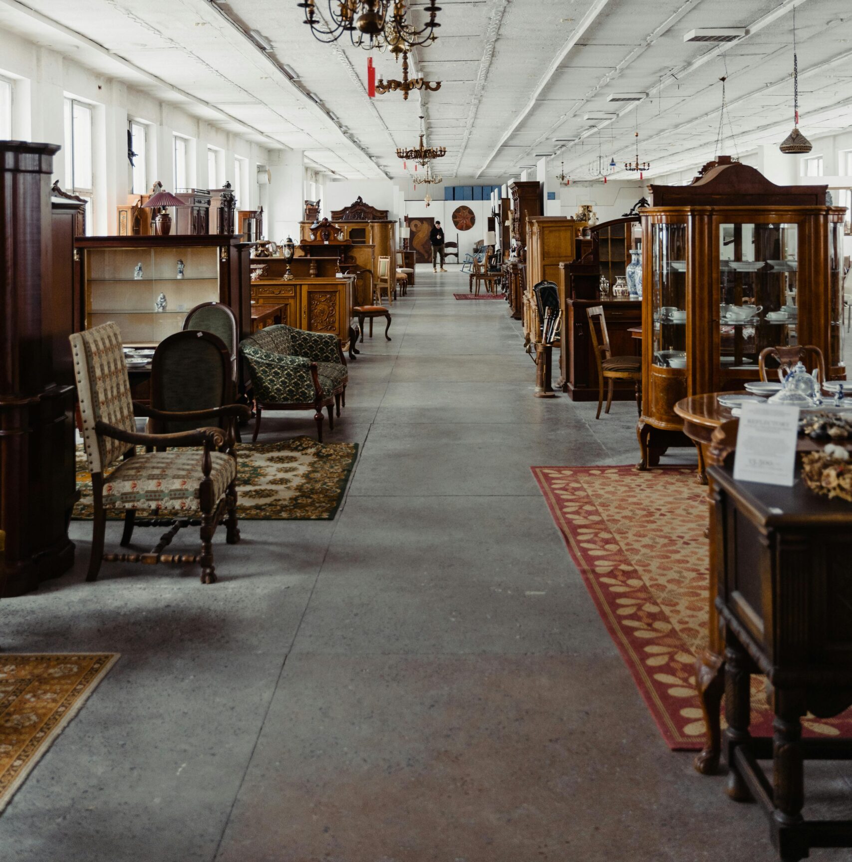 A long aisle in a vintage furniture store showcasing antique wooden pieces and chandeliers.